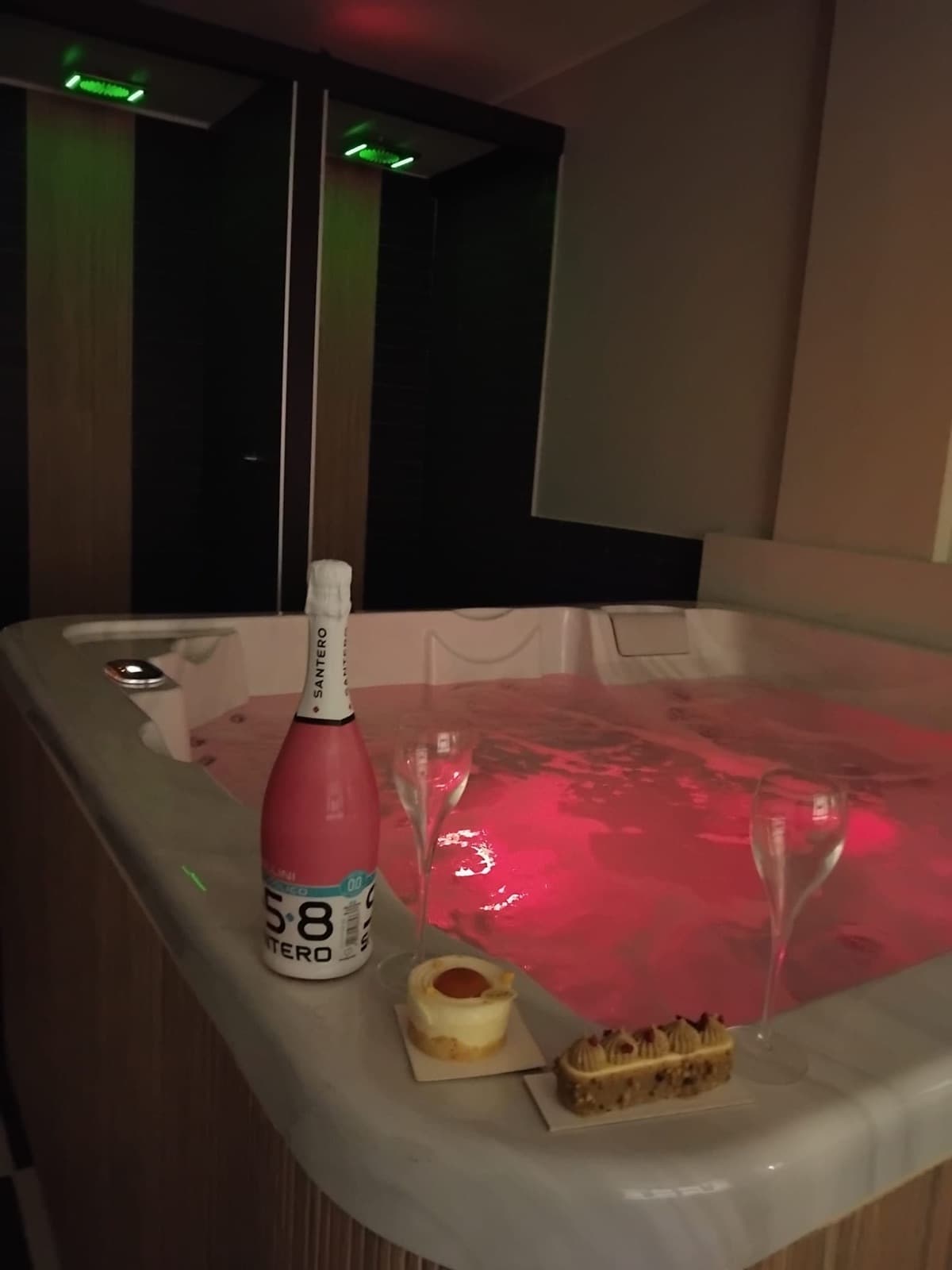 Bottiglia di prosecco rosé, calici e dolcetti a bordo della vasca idromassaggio
