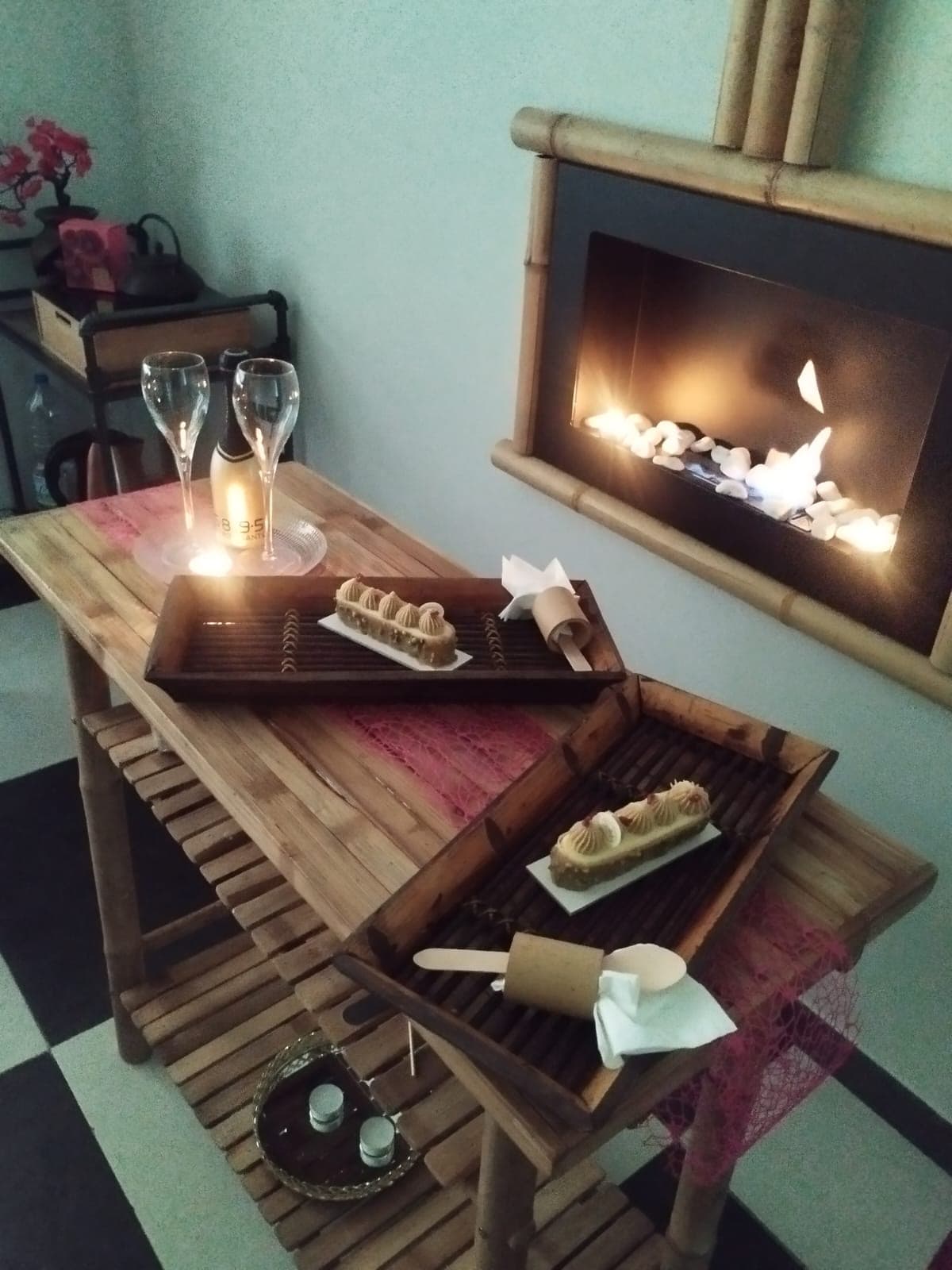 Tavolo in bambù apparecchiato con calici di prosecco e dolci davanti al camino del centro benessere BAMBÙ